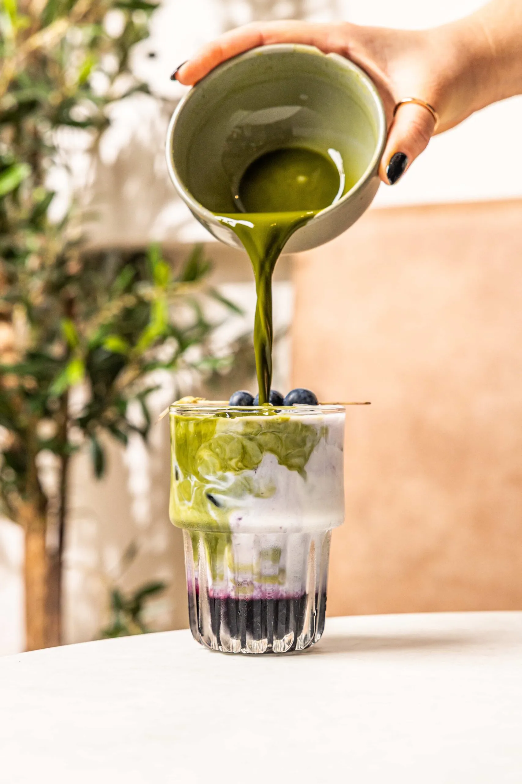 Matcha being poured from a ceramic jug into an iced blueberry matcha latte